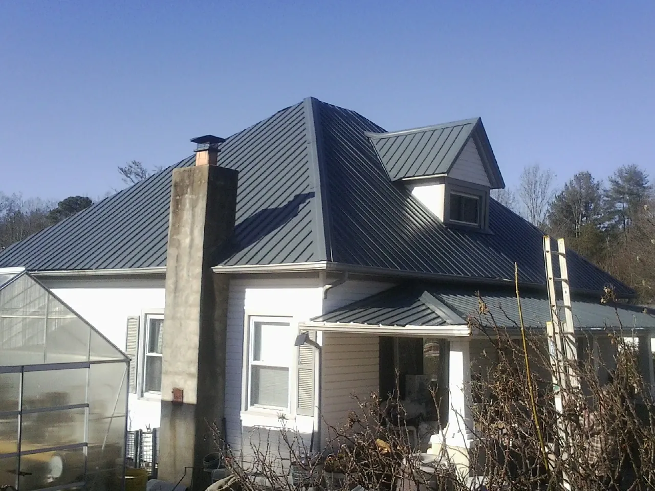 Dark blue standing seam metal roof on a white farmhouse with dormer — Slate & Tile Roof Repair by Roofing Brothers in Ronda