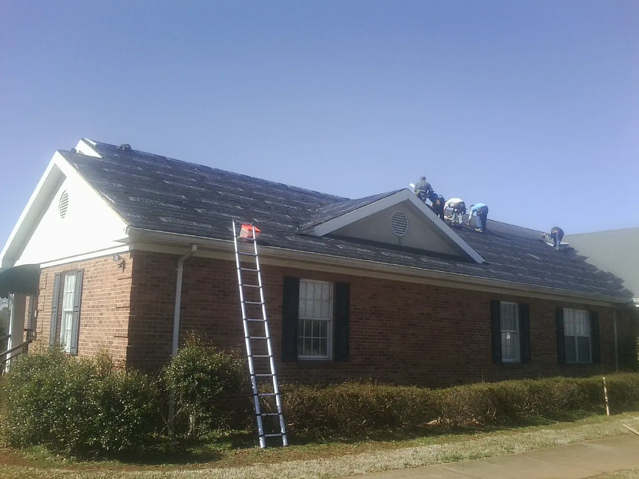 Crew tearing shingles off a brick ranch roof with a ladder set — Emergency Roof Repair work by our crew in Ronda