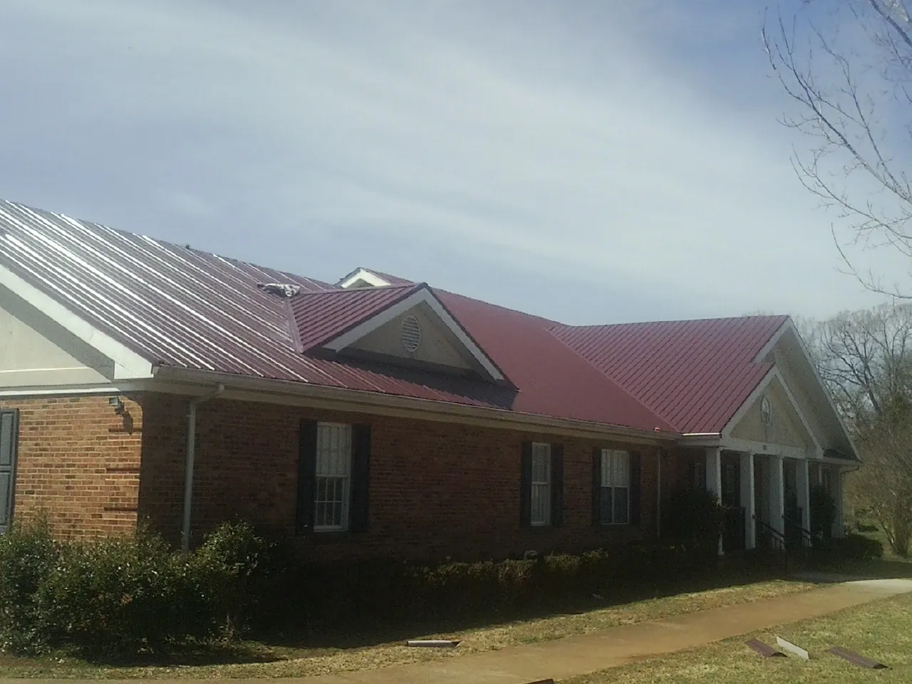 Red metal roof with gabled entries on a long brick building, from a Hail Damage Roof Repair job in Ronda