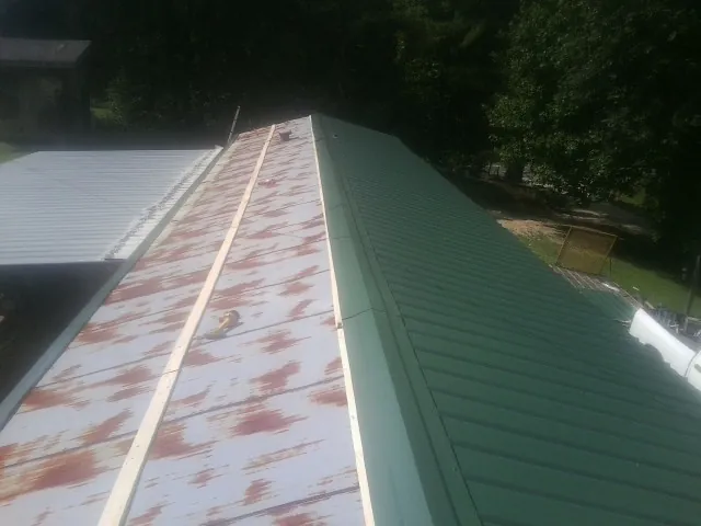 Old rusted panels beside newly installed green metal roofing — Wind Damage Roof Repair by Roofing Brothers in Ronda