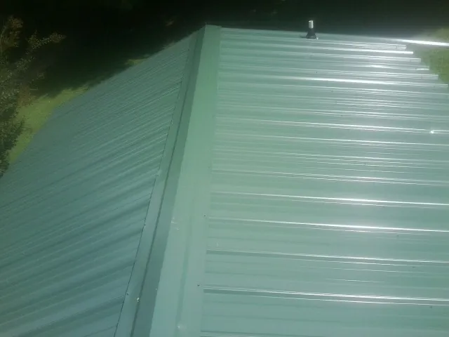 New green metal panels meeting at the ridge of a roof — Flat Roof Repair work by our crew in Ronda