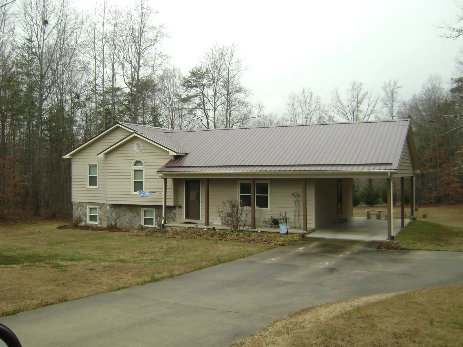 Brown metal roof on a tan split level home with an attached carport in Ronda