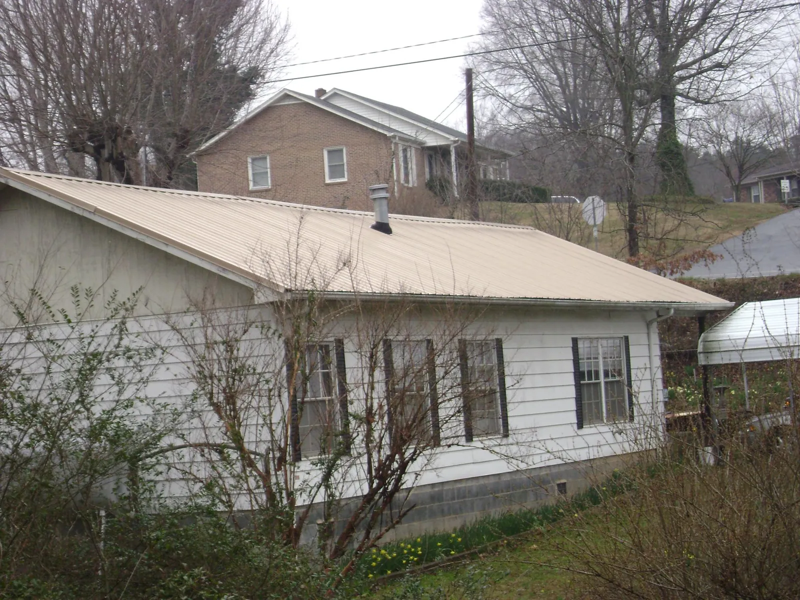 Tan metal roof on a white sided house set into a hillside — Commercial Roofing by Roofing Brothers in Ronda
