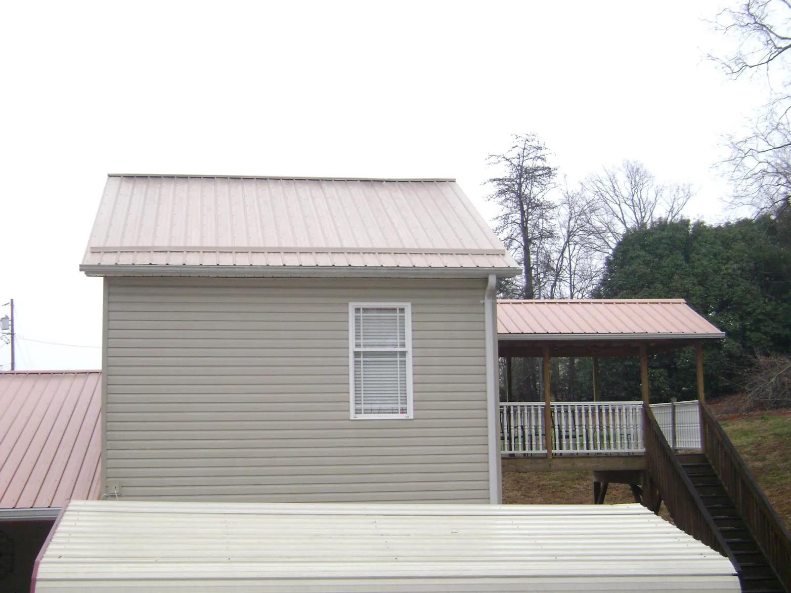 Tan metal roofs on a two story addition and attached porch, from a Roof Replacement job in Ronda